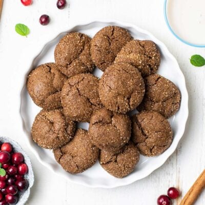Soft and chewy ginger cookies shown in a serving dish surrounded by cranberries and cinnamon sticks.