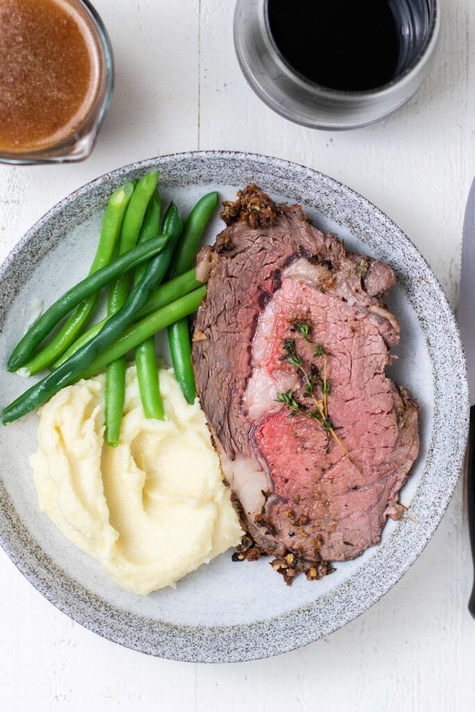A slice of prime rib served with potatoes and green beans.