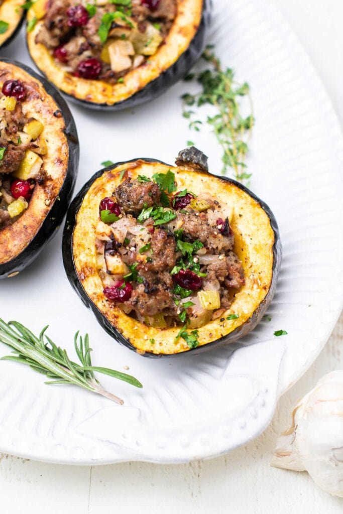 A white platter with sausage stuffed acorn squash.
