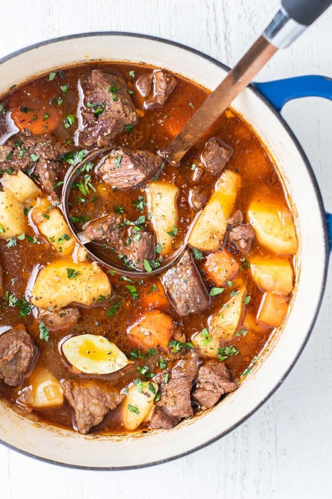 A hearty beef stew shown with a ladle in a pot.