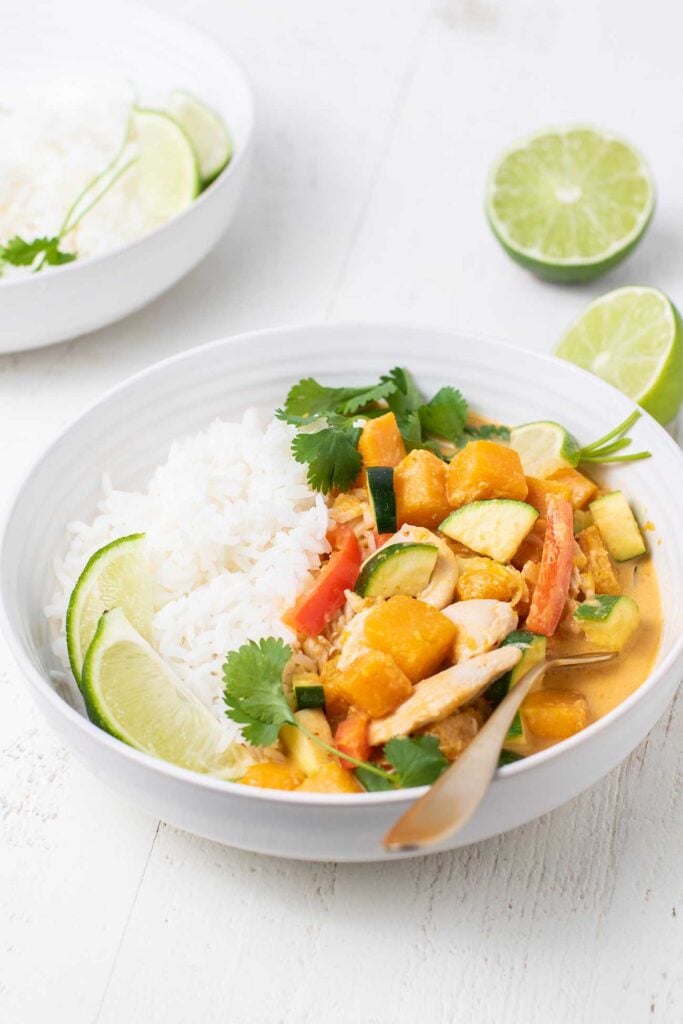 A red curry shown served on rice with cilantro and lime.