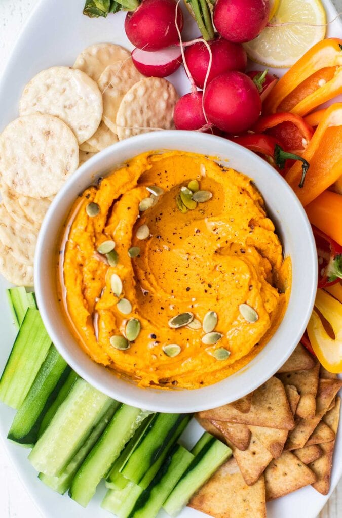 A bright orange carrot hummus garnished with olive oil and pumpkin seeds.