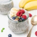 A jar of chia pudding shown topped wtih bananas, nuts, seeds and berries.