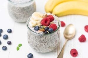 A jar of chia pudding shown topped wtih bananas, nuts, seeds and berries.