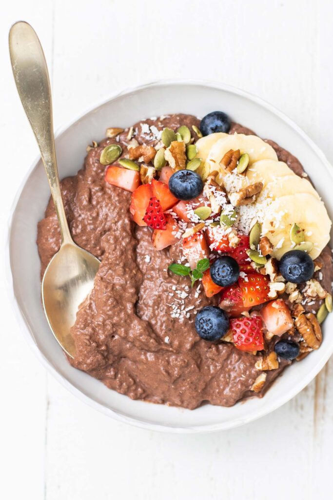 A bowl of chocolate chia seed pudding topped with fruit, nuts, and coconut.