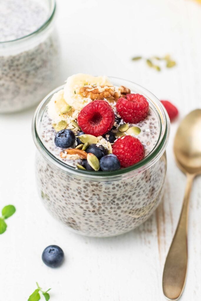 A jar of chia seed pudding topped with bananas, raspberries, and pecans.