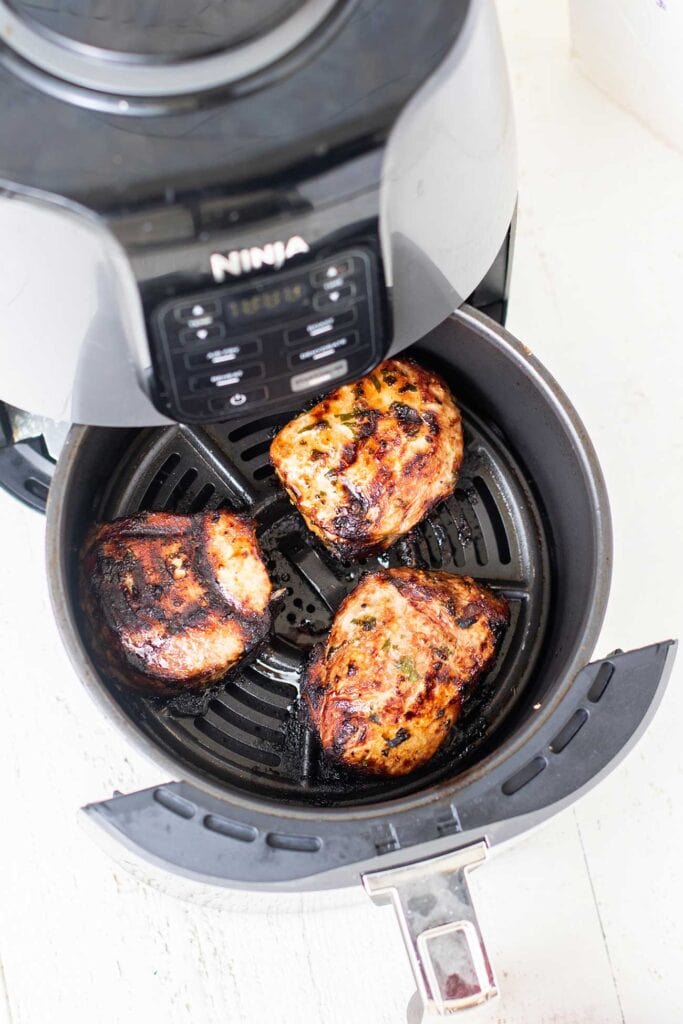 An air fryer shown with perfectly glazed pork chops inside.