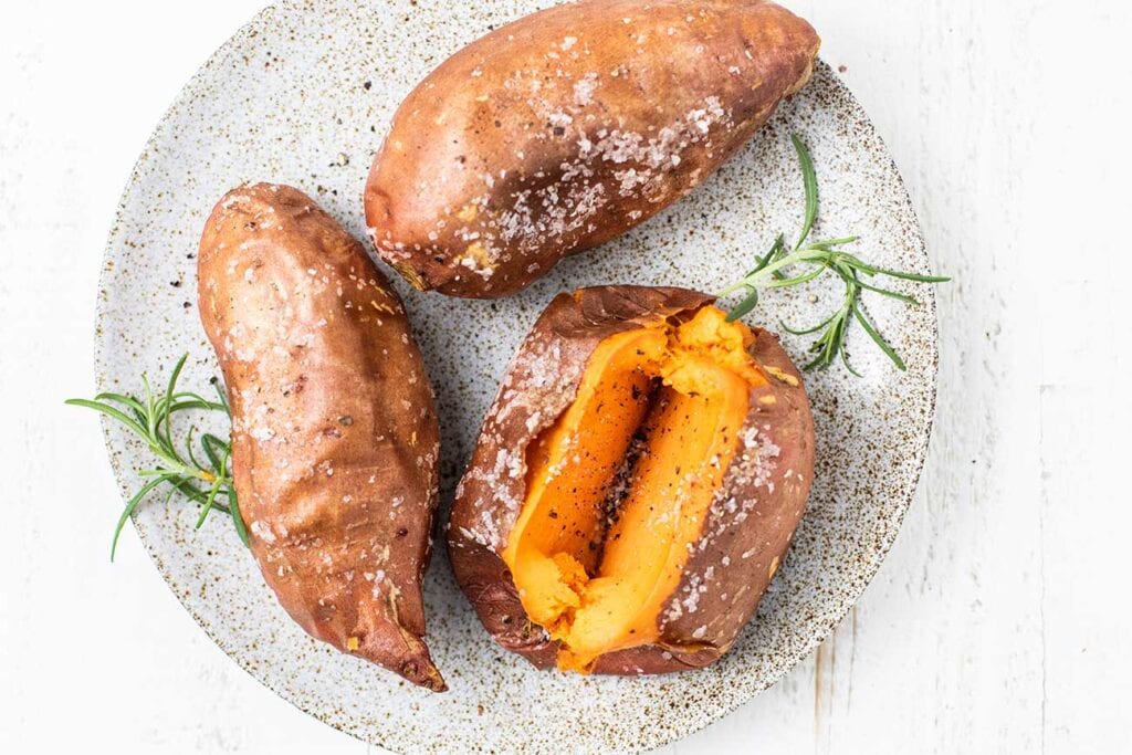 A plate of air fryer sweet potatoes shown garnished with salt, pepper, and rosemary.