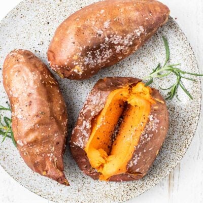 A plate of air fryer sweet potatoes shown garnished with salt, pepper, and rosemary.