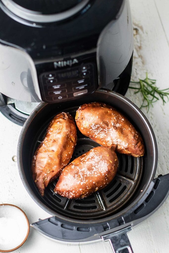 A Ninja air fryer shown with baked sweet potatoes in the frying basket.
