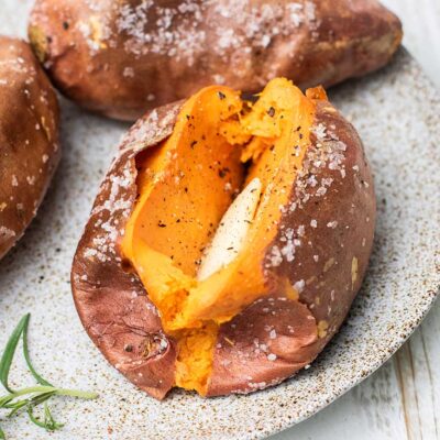 Perfectly baked sweet potatoes prepared in an air fryer shown with butter, salt and pepper.