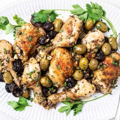 A platter with roasted chicken, olives, and prunes.