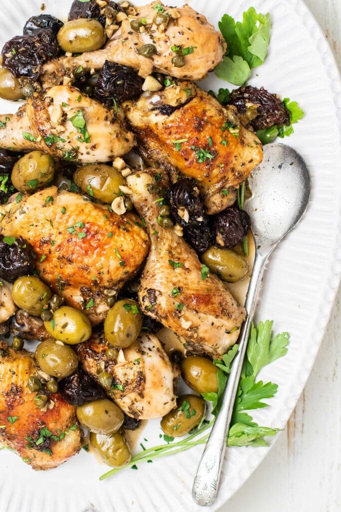 A close up of a platter of chicken garnished with olives and prunes.