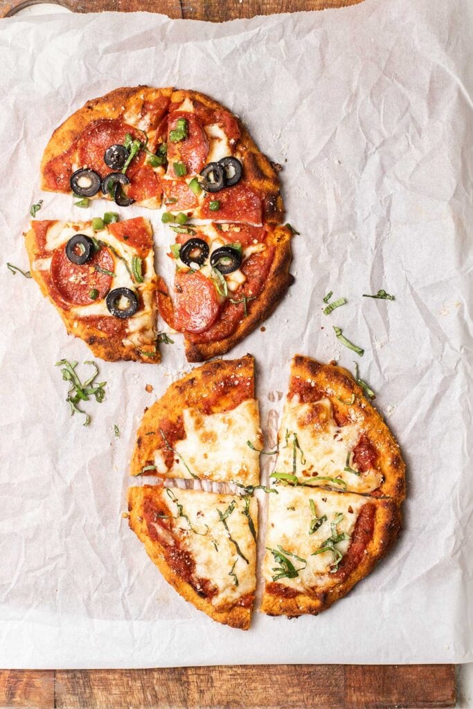Two sweet potato pizzas shown sliced and garnished with basil and chili flakes.