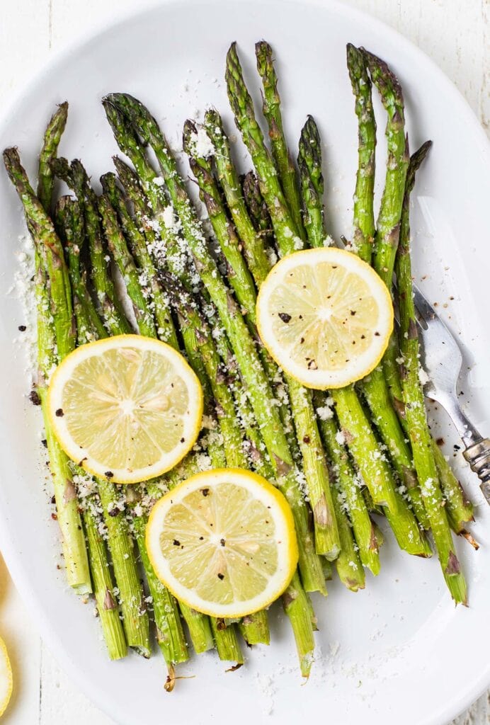 A plate with air fryer asparagus garnished with lemon slices and parmesan cheese.