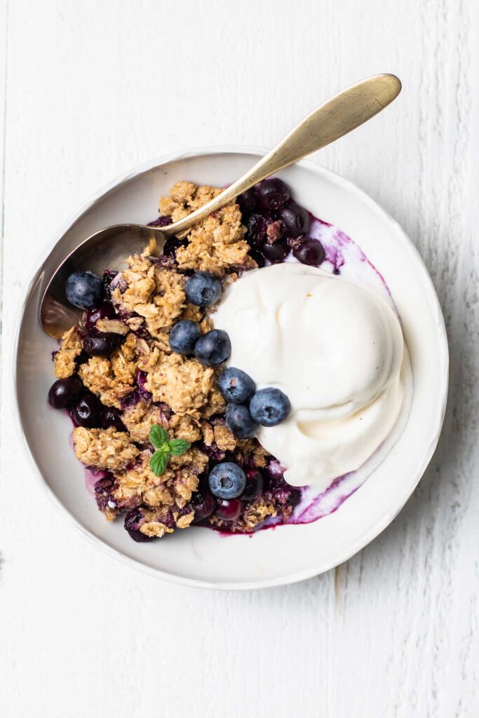 A bowl with a serving of blueberry crisp, topped with melty vanilla ice cream.