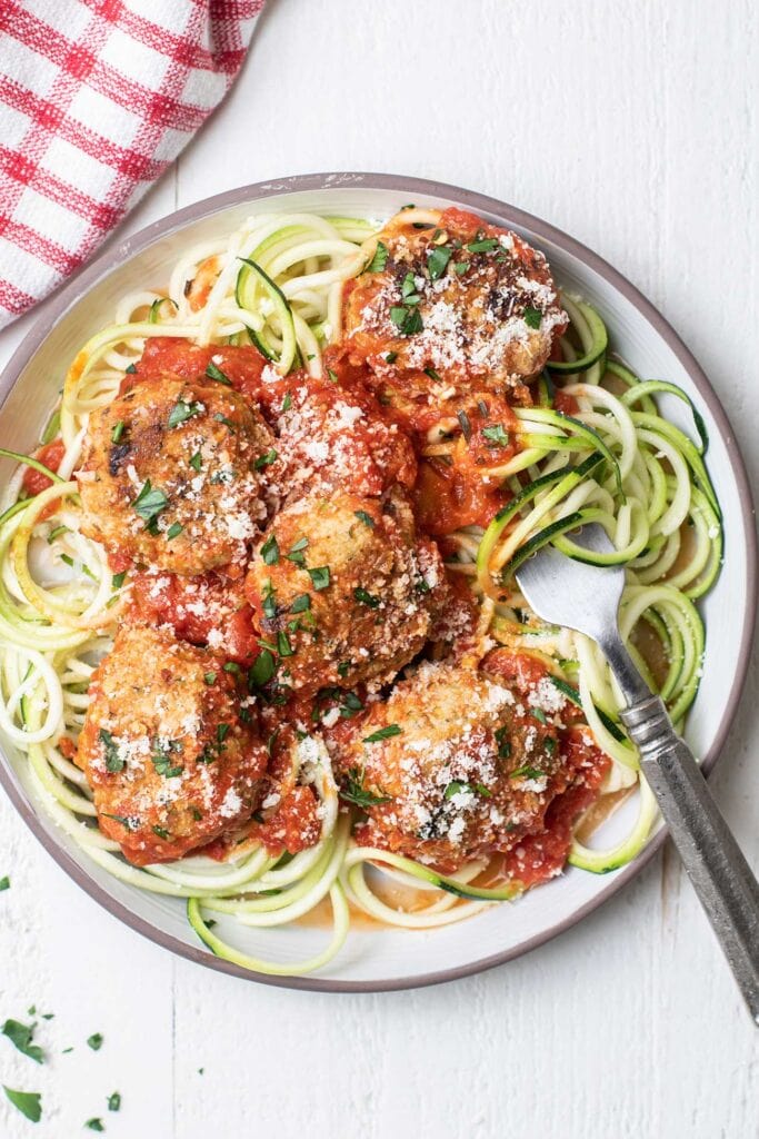 A plate with zoodles and healthy chicken meatballs served with marinara sauce and parmesan cheese.