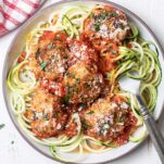A plate with a serving of zoodles, topped by gluten free chicken meatballs.