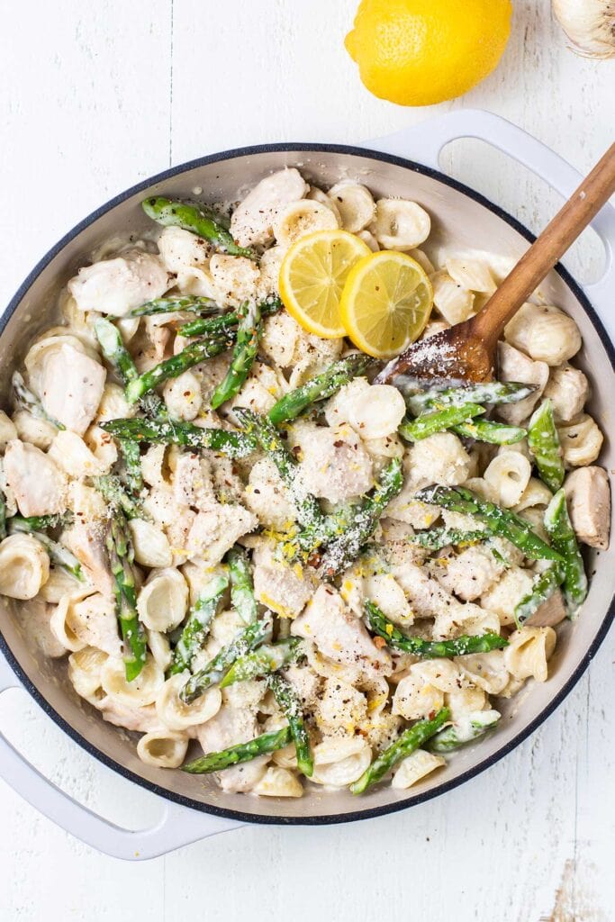 A white pot filled with a creamy pasta with asparagus and chicken.