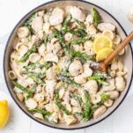 A creamy pasta dish with asparagus and chicken shown in a white pot.