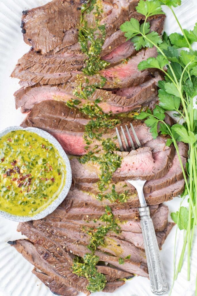 A sliced london broil shown drizzled with chimichurri.