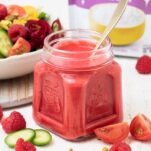 A bright pink salad dressing in a jar sitting in front of a colorful salad.