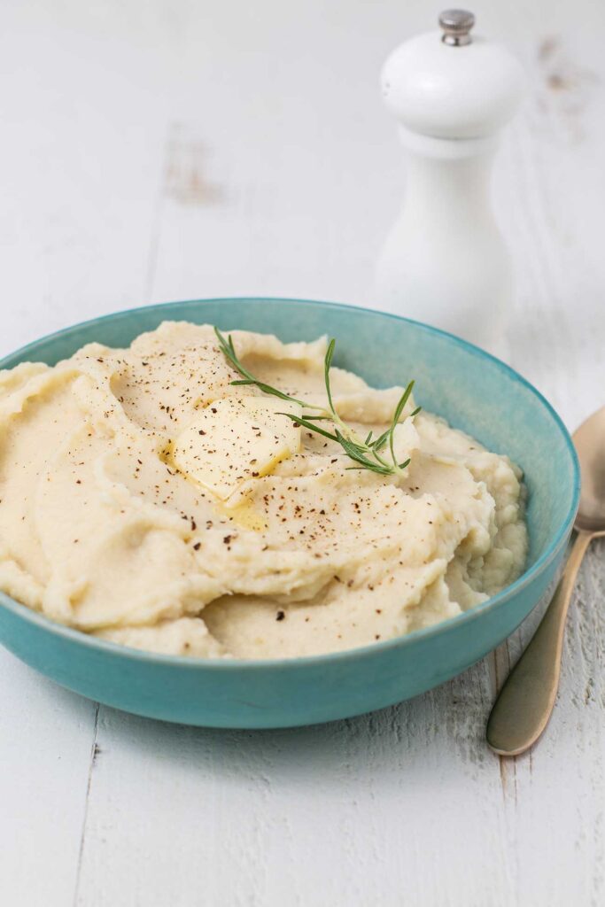 A bowl of cauliflower puree shown topped with butter and rosemary.