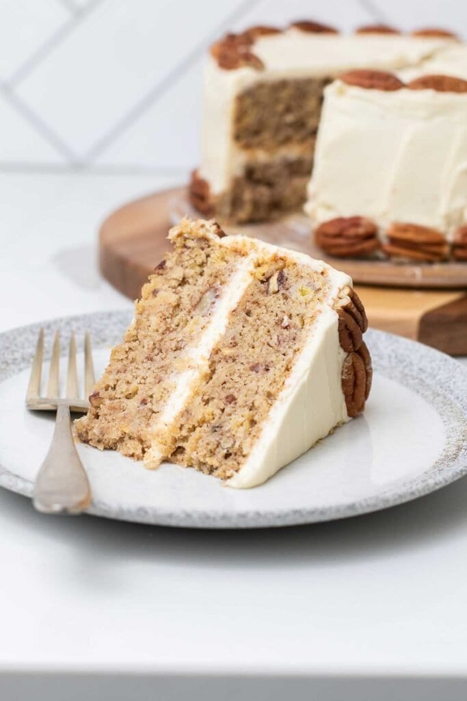 A slice of healthy hummingbird cake topped with cream cheese frosting and pecans.