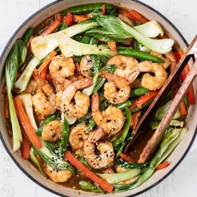 A close up look at a shrimp stir fry in a skillet with a dark teriyaki sauce.