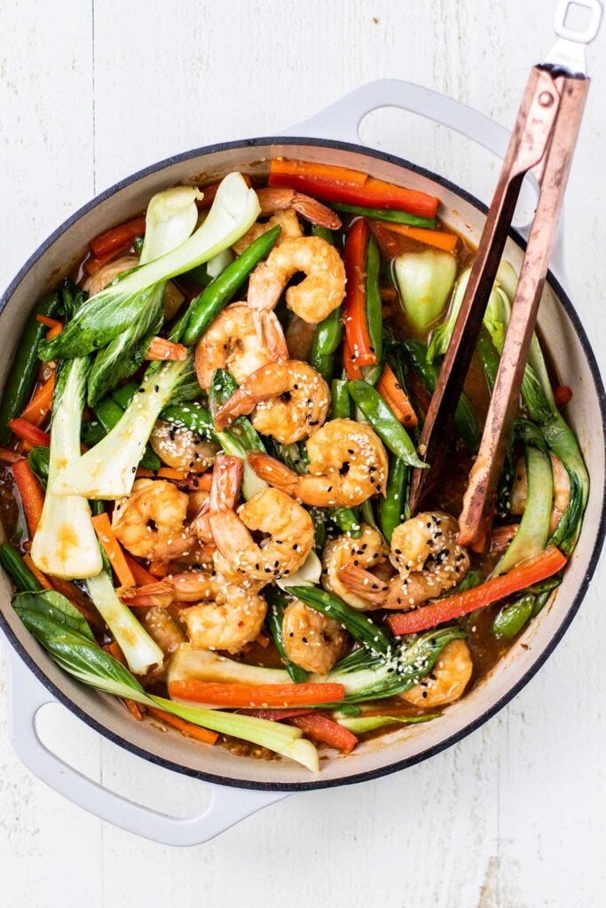 A teriyaki shrimp stir fry shown in a white cast iron pan.