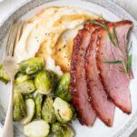 A plate with mashed cauliflower, brussels sprouts, and honey baked ham, drizzled with a ham gravy.
