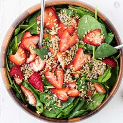 A top down look at a spinach salad topped with strawberries and seeds.