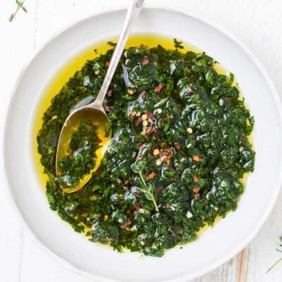 A close up look at a white bowl filled with a vibrant green chimichurri sauce.