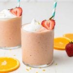 Two strawberry smoothies shows with whole oranges and strawberries.