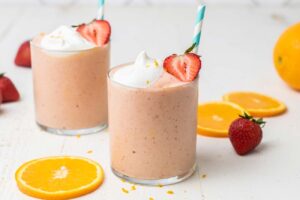 Two strawberry smoothies shows with whole oranges and strawberries.