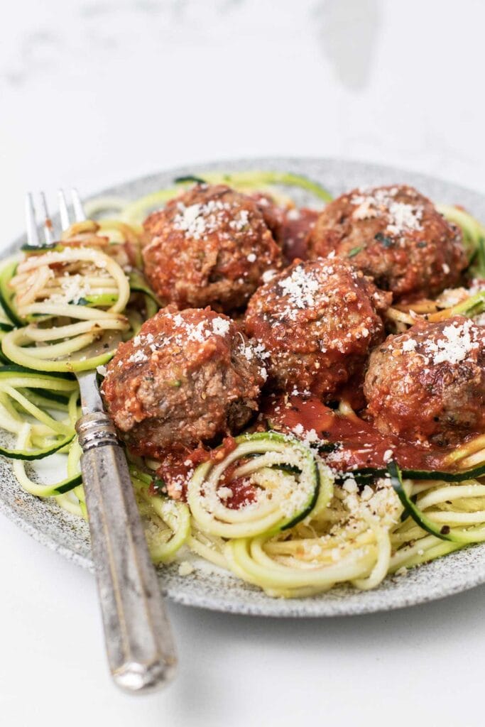 Meatballs and marinara sauce served over a plate of zucchini noodles.