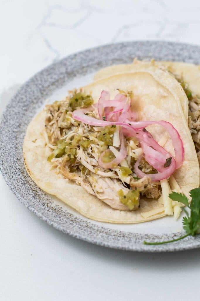 A corn tortila with salsa verde chicken and pickled red onions.