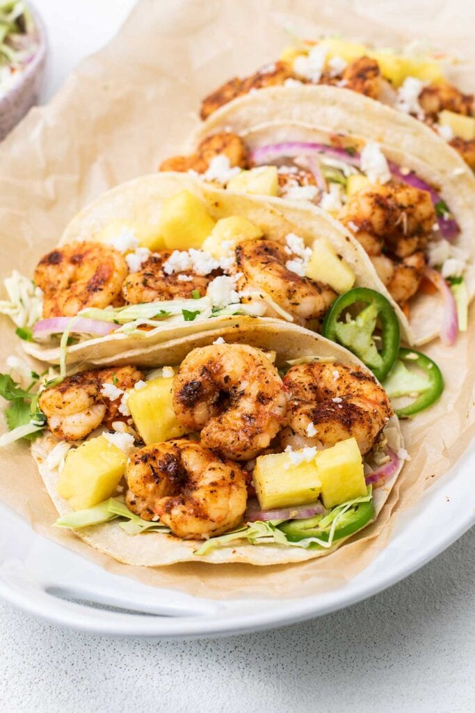 A platter of shrimp tacos shown garnished with pineapple and jalapeno.