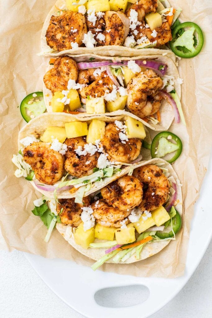 A platter of shrimp tacos showing the chunks of pineapple and the cabbage slaw.