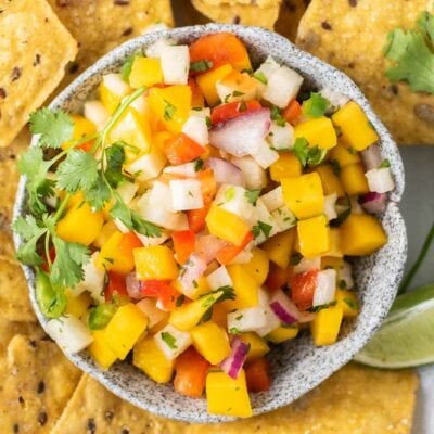 A close up look at a brightly colored mango salsa served with chips.