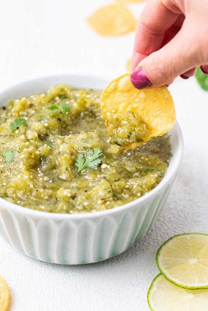 A tortilla chip dipping in to a bowl of salsa verde.