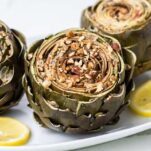A look at a platter of stuffed artichokes shown served with lemon wedges.