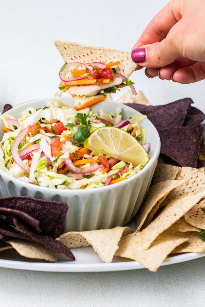 A chip dipping in to a bowl of Mexican cabbage salsa.