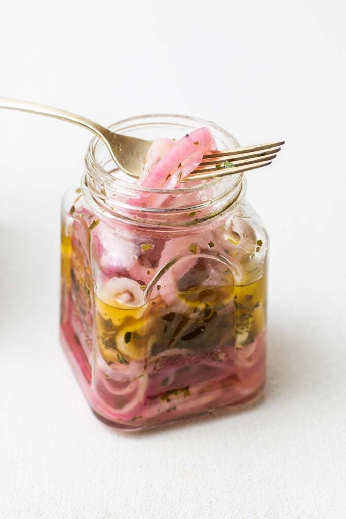 A jar filled with marinated red onions with a fork pulling some onions out of the top.