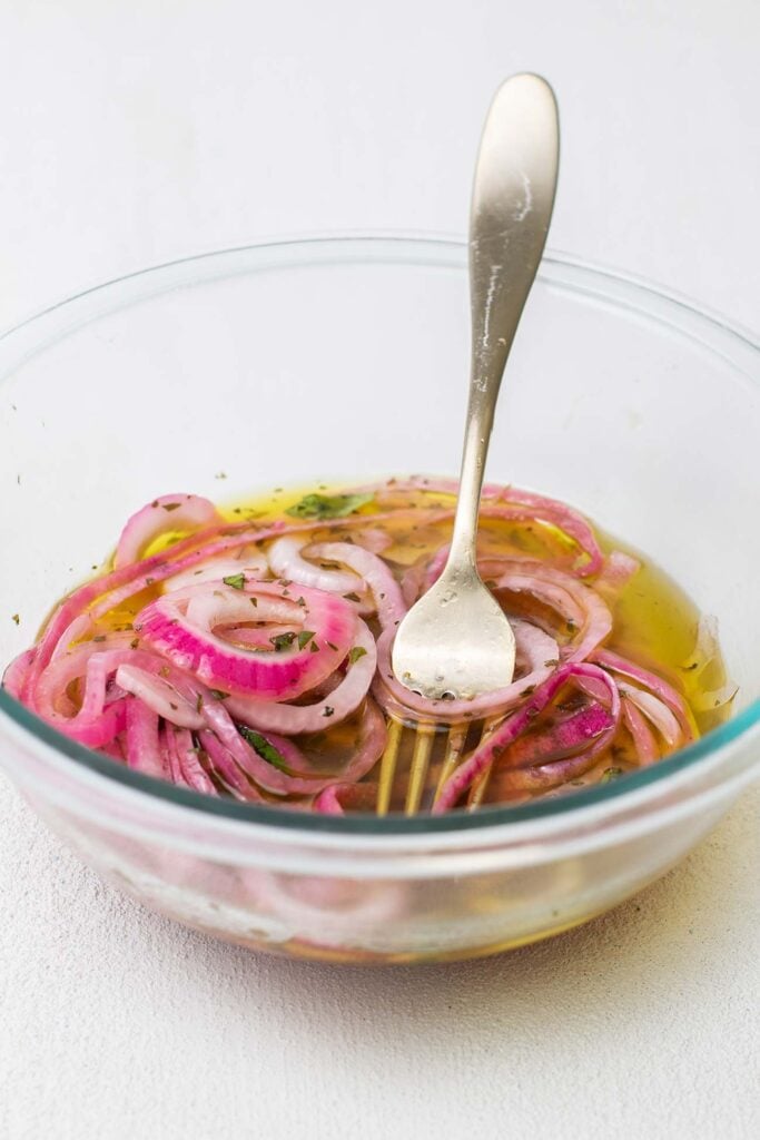 A bowl shown with red onions marinating in vinegar and olive oil.