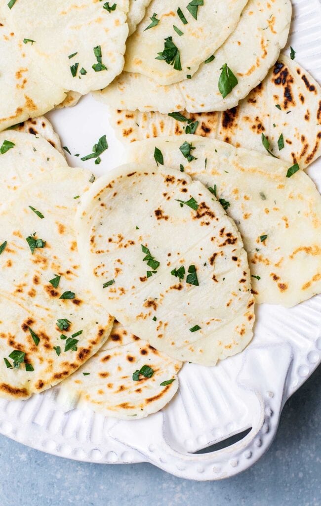 A white platter with gluten free flatbread garnished with parsley.