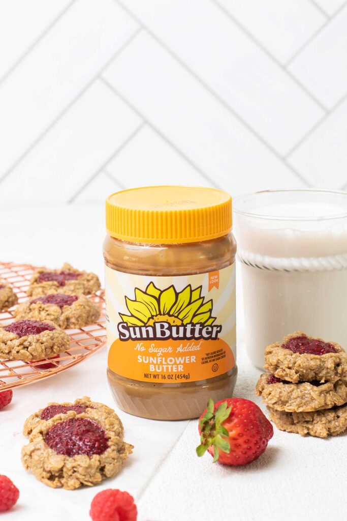 A jar of SunButter sitting with thumbprint cookies on a cooling rack.