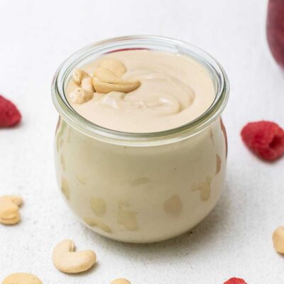 A jar filled with cashew butter sitting in front of a jar of raspberry jam.