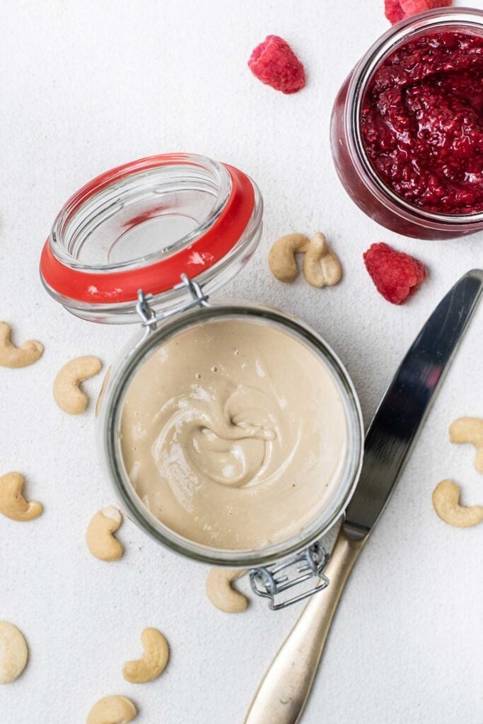 A jar of nut butter sitting with a jar of raspberry chia jam.