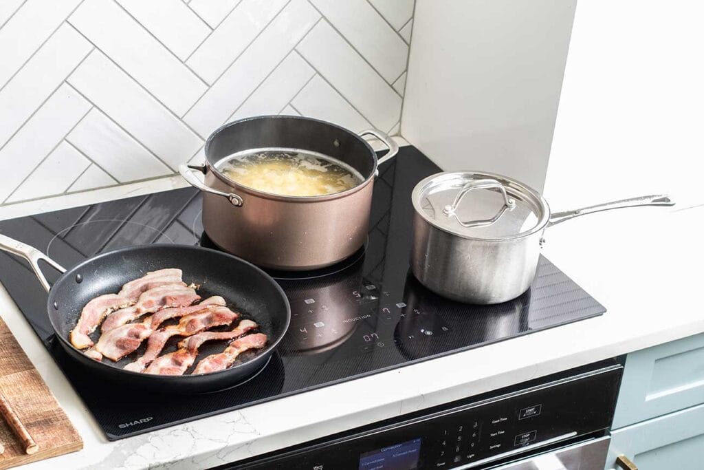 The Sharp Induction Cooktop shown with boiling pasta, a pan of bacon, and a saucepan with eggs.